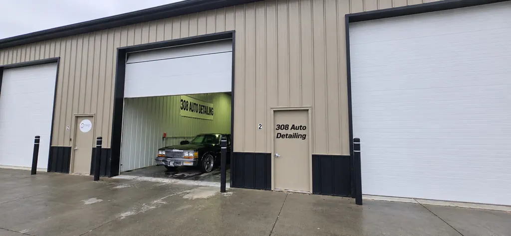Front of the 308 Auto Detailing shop on Bronze Rd: a tan metal building with an open bay door, a 308 Auto Detailing sign inside and a black classic car being washed